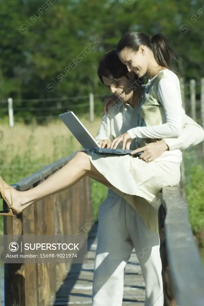 Couple on footbridge using laptop