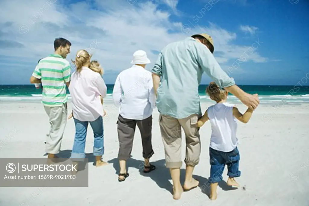 Three generation family walking on beach, rear view