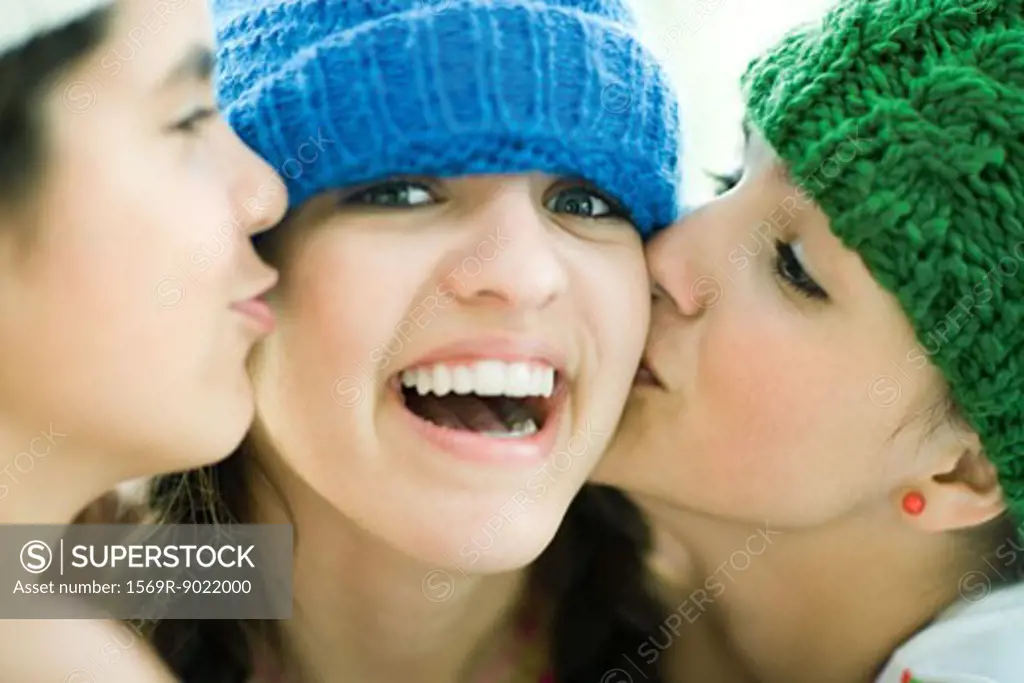 Young female being kissed on cheeks by two friends, smiling at camera