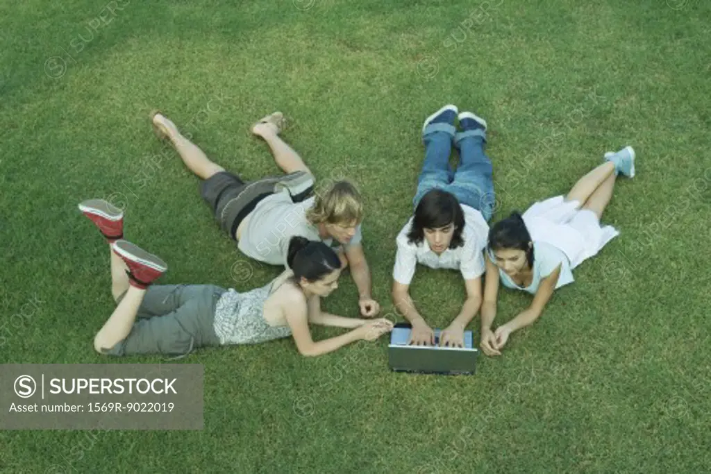 Group of young friends lying on grass, using laptop
