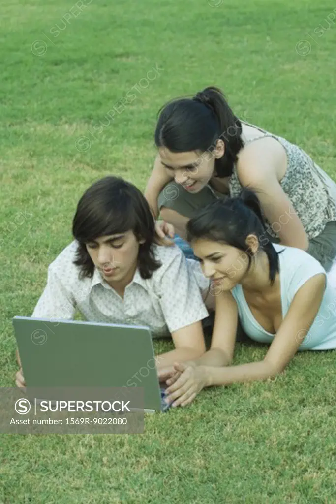 Group of young friends lying in grass using laptop