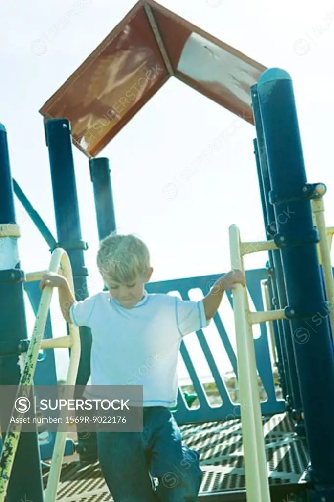 Boy on playground equipment, holding onto railing