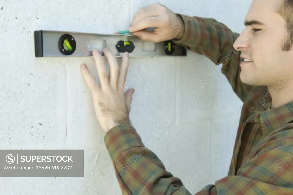 Man using level to draw line on wall