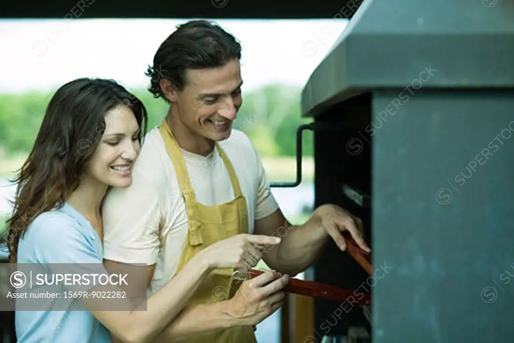 Couple having cookout together, woman pointing to barbecue
