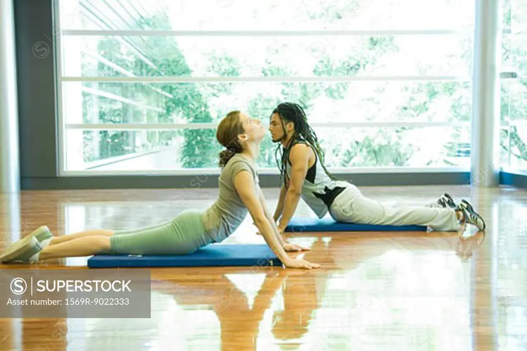 Two young adults doing cobra pose in yoga studio