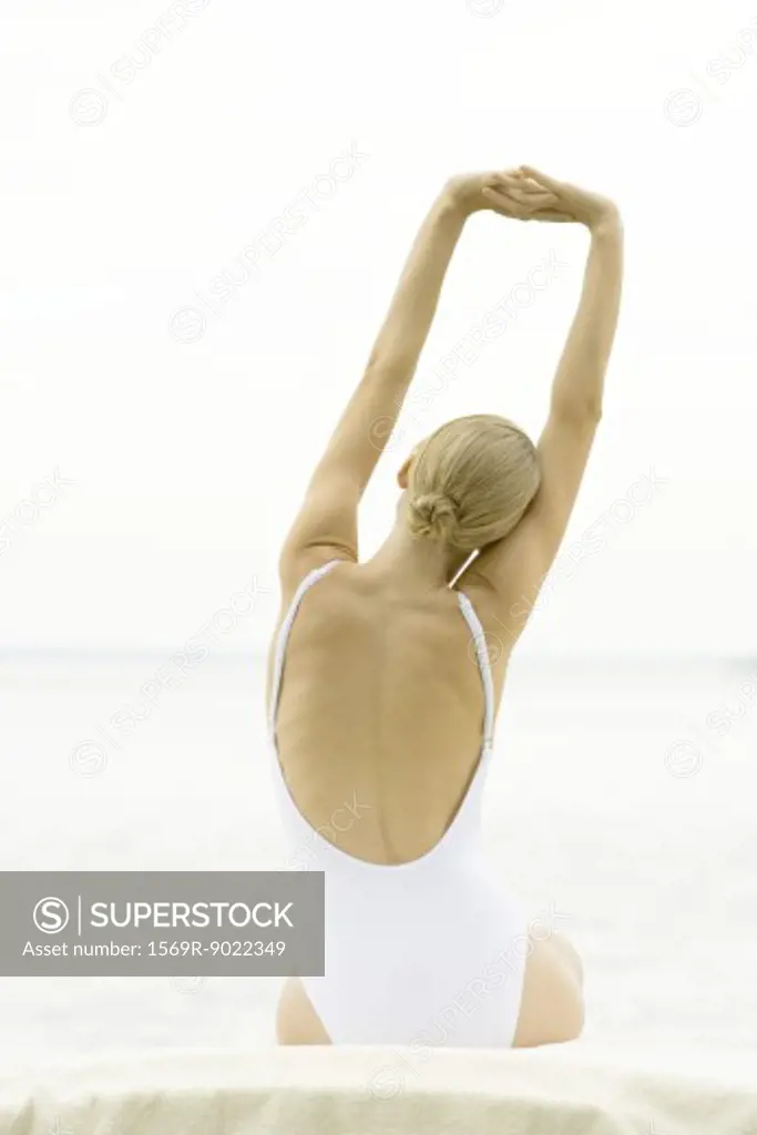 Teenage girl sitting stretching arms, wearing bathing suit, rear view