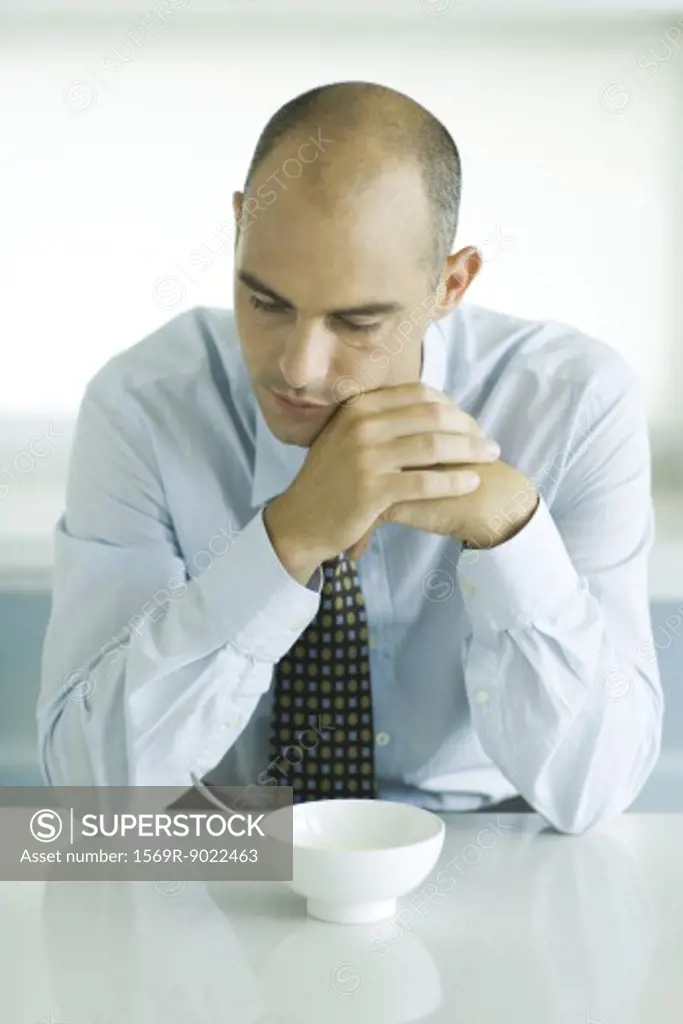 Man sitting at table with empty bowl in front of him