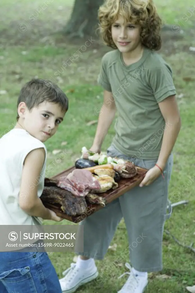 Two boys carrying tray of grilled and raw meats