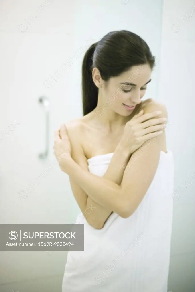 Young woman wrapped in towel, arms crossed and hands on shoulders