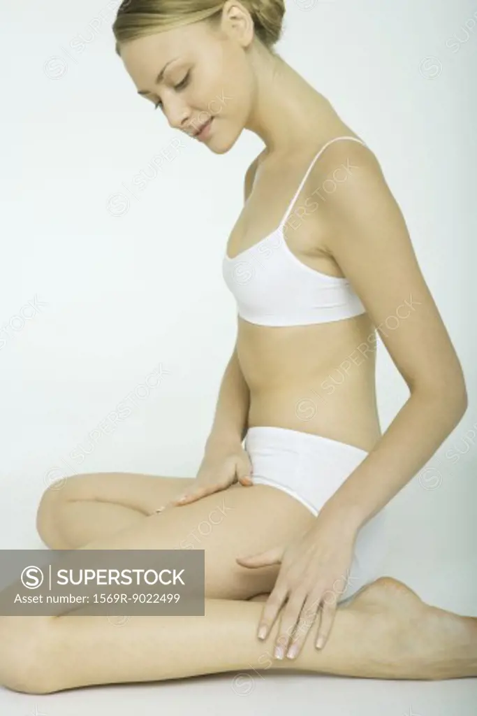 Young woman sitting on knees, looking at legs