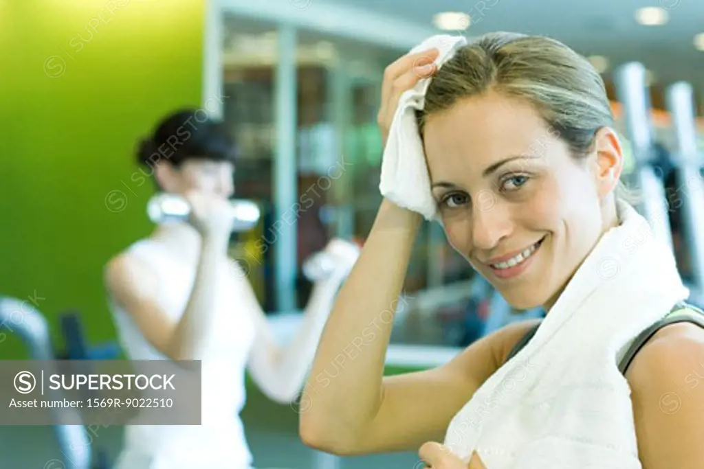 Woman in weight room, wiping forehead, smiling at camera