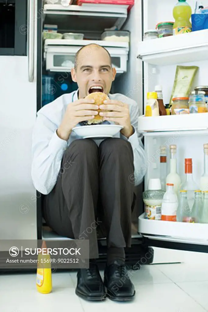 Man sitting inside refrigerator, eating sandwich
