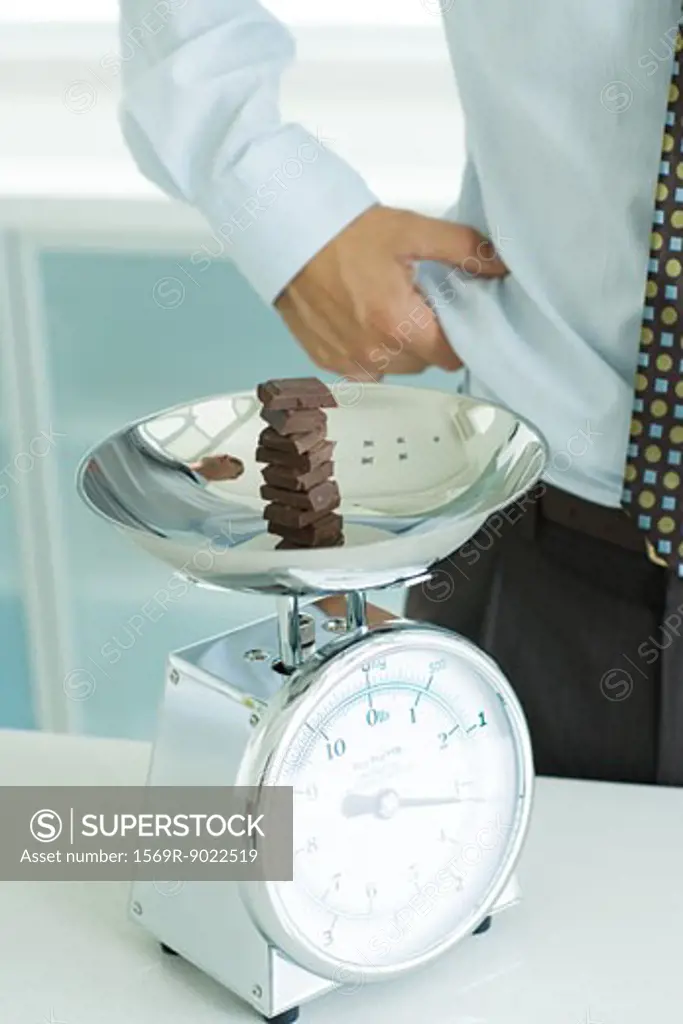 Stack of chocolate chunks on kitchen scale, and man pinching waist