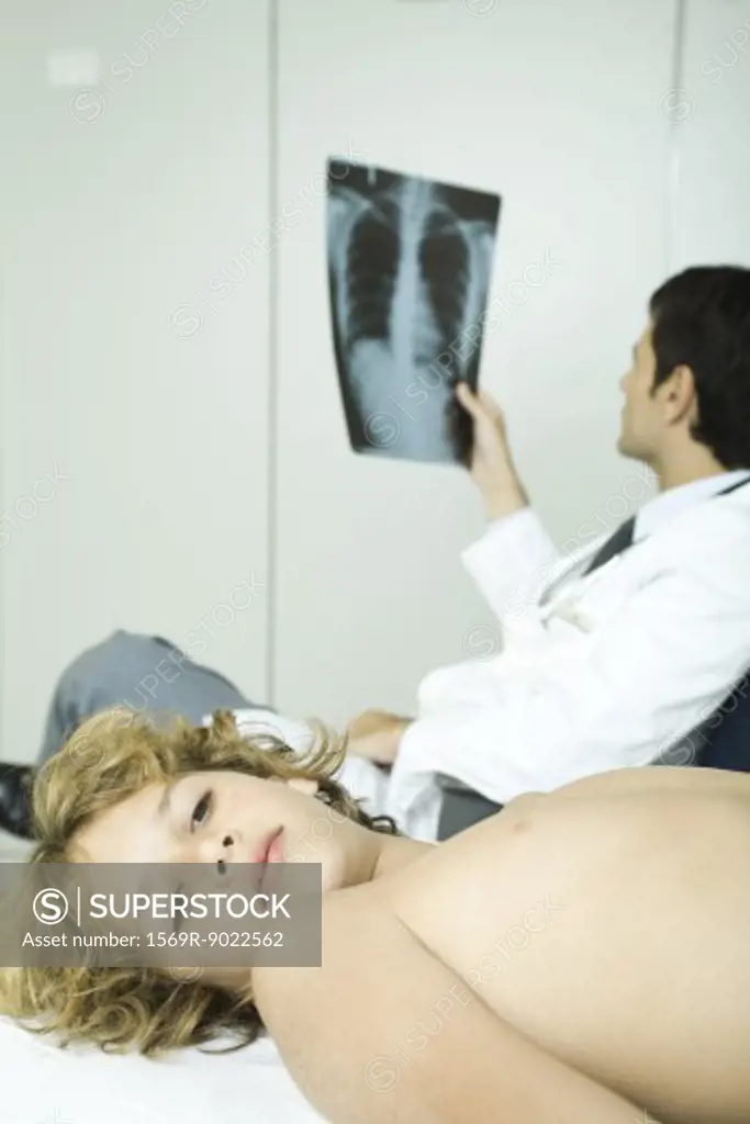 Boy lying down in doctor's office while doctor looks at x-ray