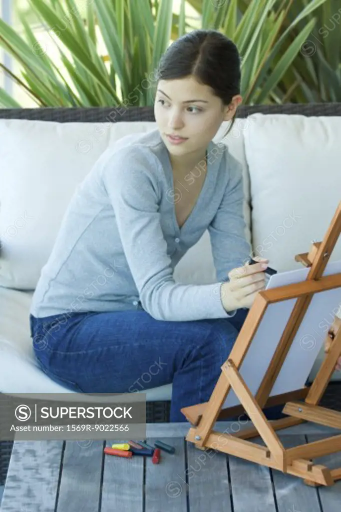 Young woman sitting with easel, drawing with pastels