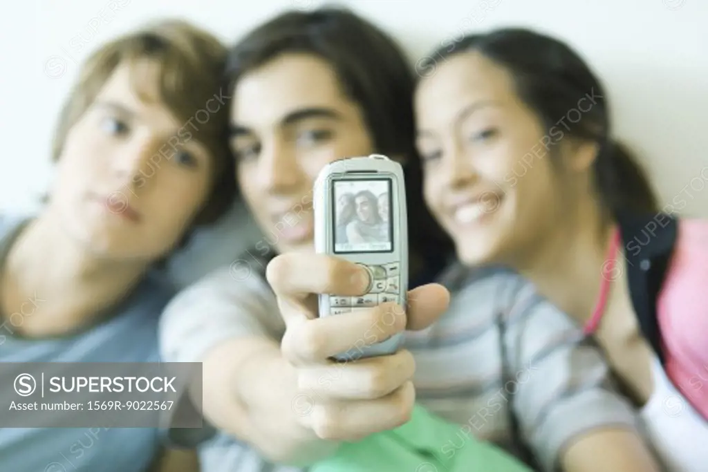 Teenage friends taking photo with cell phone, focus on phone in foreground