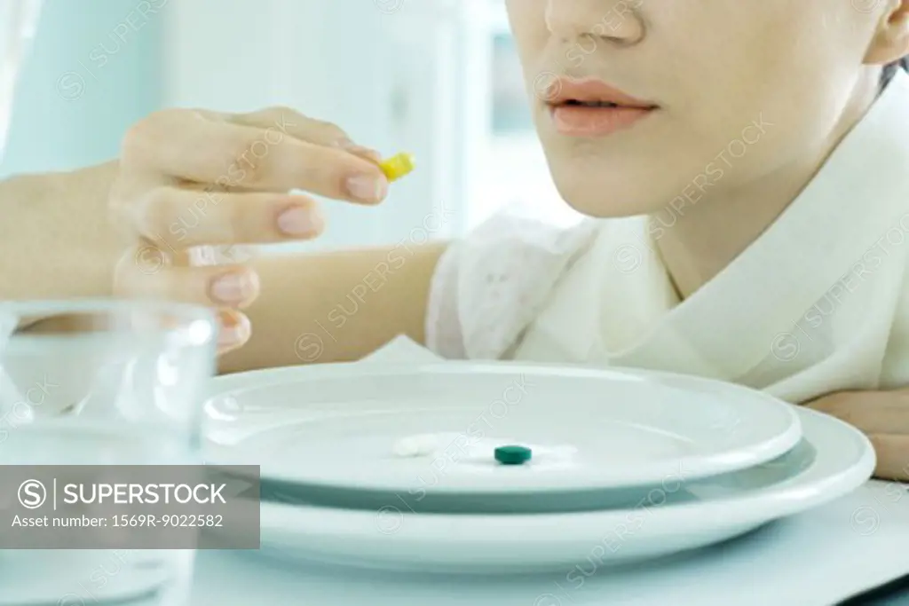 Woman sitting at set table, eating vitamins from plate