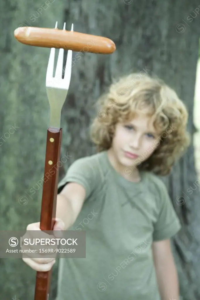 Boy holding hot dog on end of large fork 