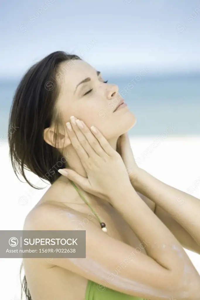 Woman with sunscreen on arm, hands on either side of face, eyes closed