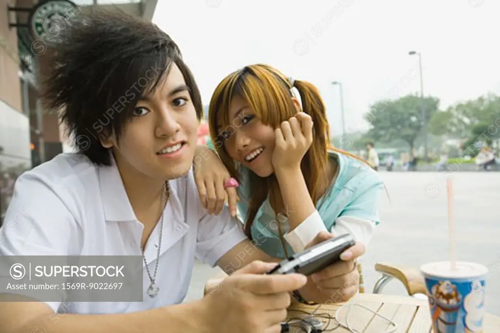 Teenage couple sitting at outdoor cafe, boy holding video game