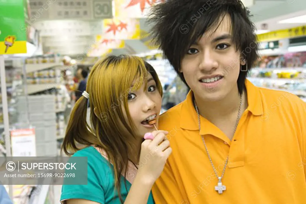 Teenage couple in grocery store, girl eating lollipop