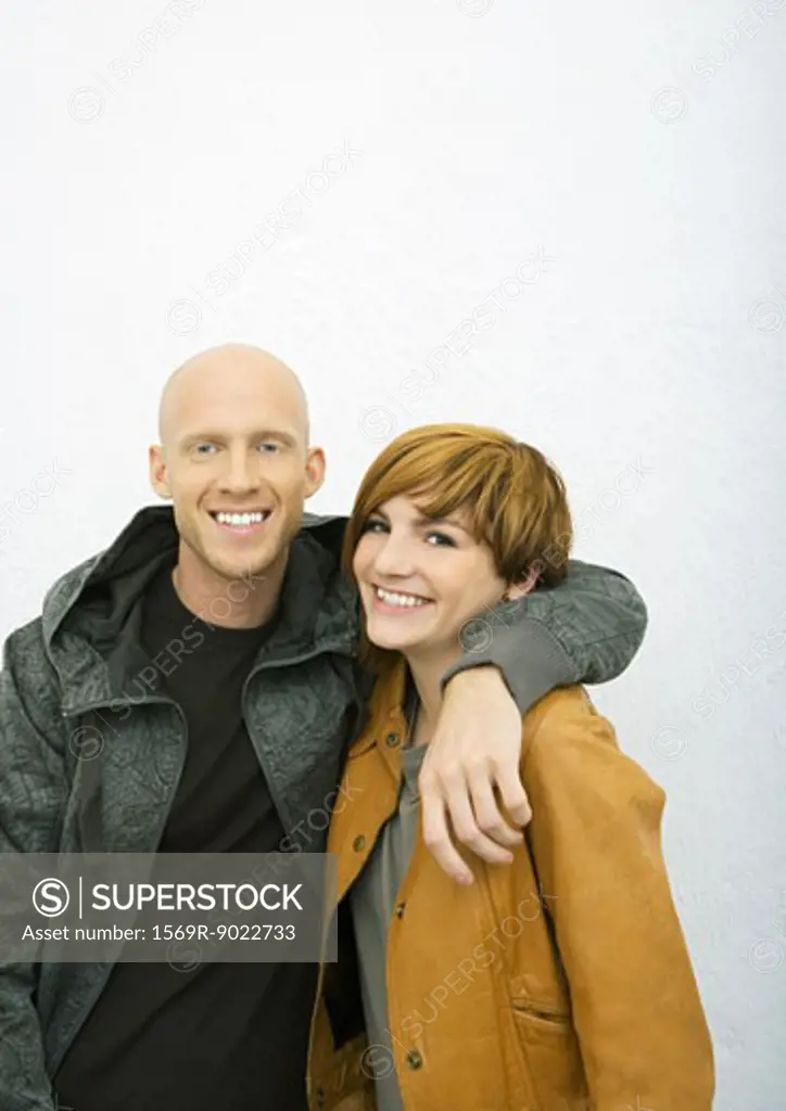 Young couple, man with arm around woman's shoulders, both smiling at camera