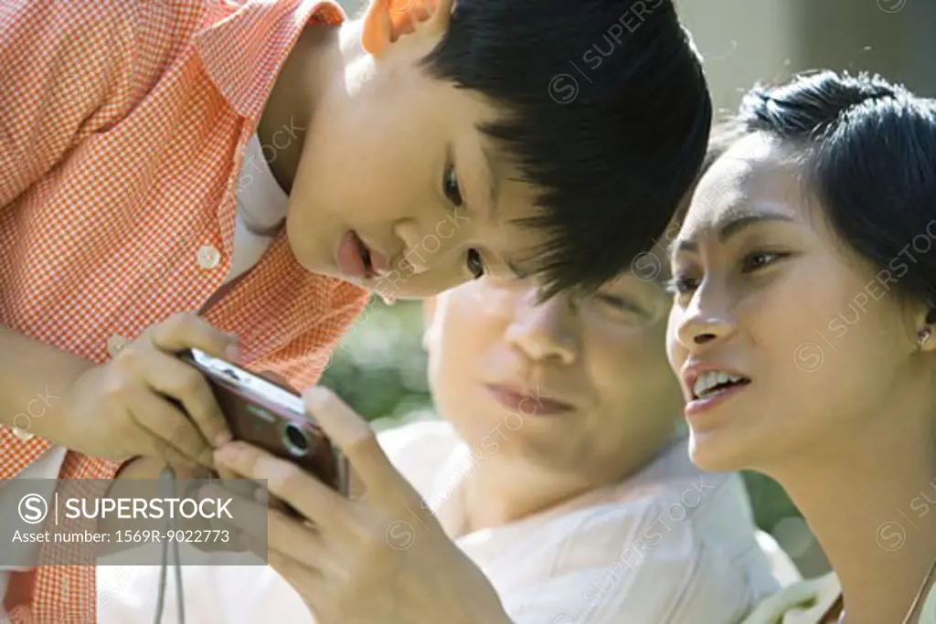 Boy with parents, mother holding digital camera, boy bending over to look