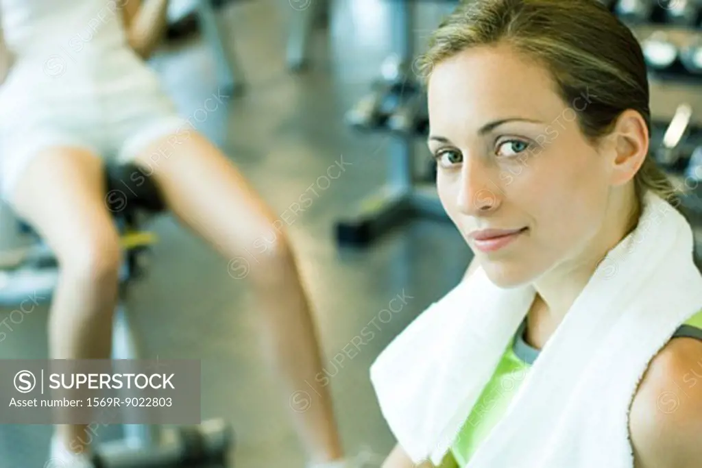 Woman in health club with towel around neck, smiling at camera