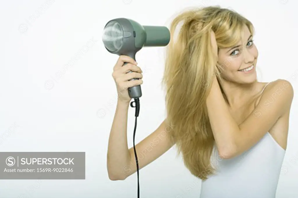 Teenage girl blow-drying hair, smiling at camera