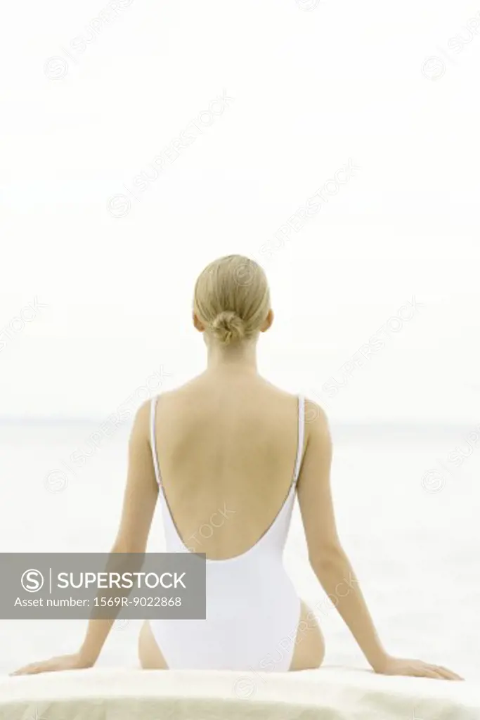 Female in bathing suit sitting on lounge chair, rear view