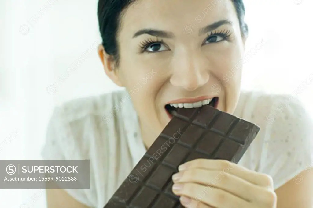 Woman taking bite out of bar of chocolate