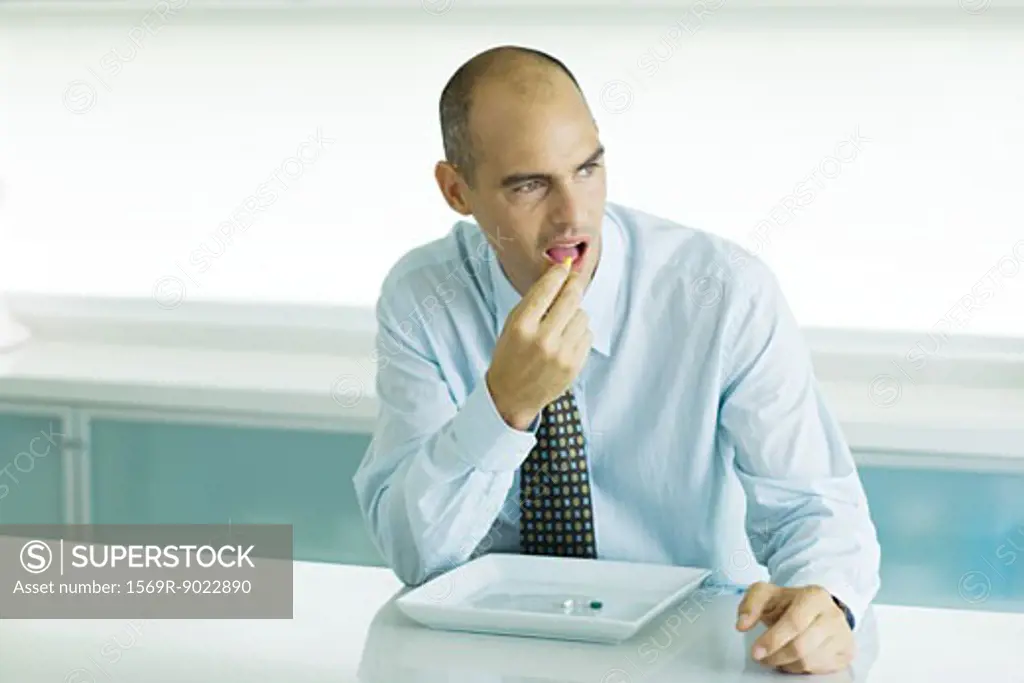 Man sitting at table eating vitamins from sparse plate