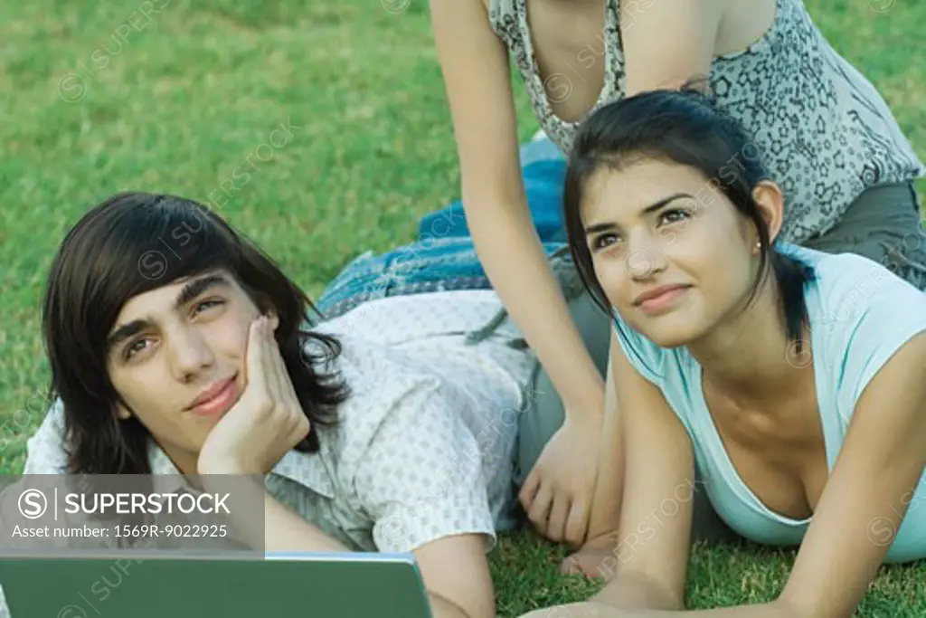 Group of young friends lying on grass using laptop