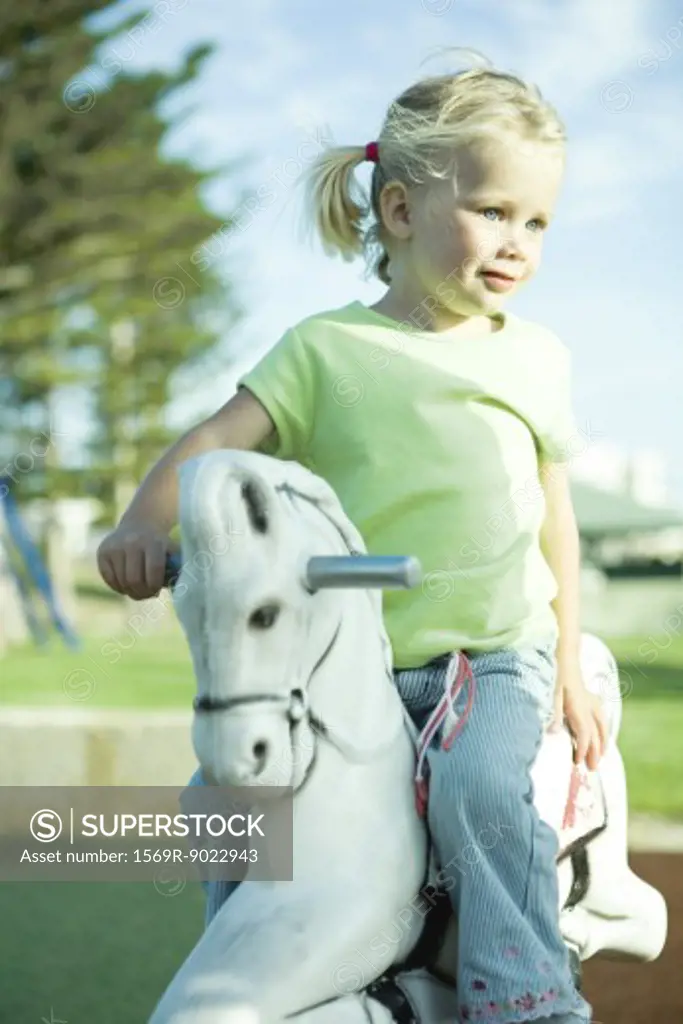 Girl on playground rocking horse, looking away 