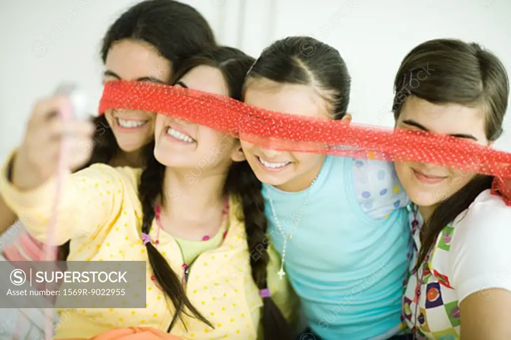 Four young female friends holding scarf in front of eyes, one taking photo with cell phone