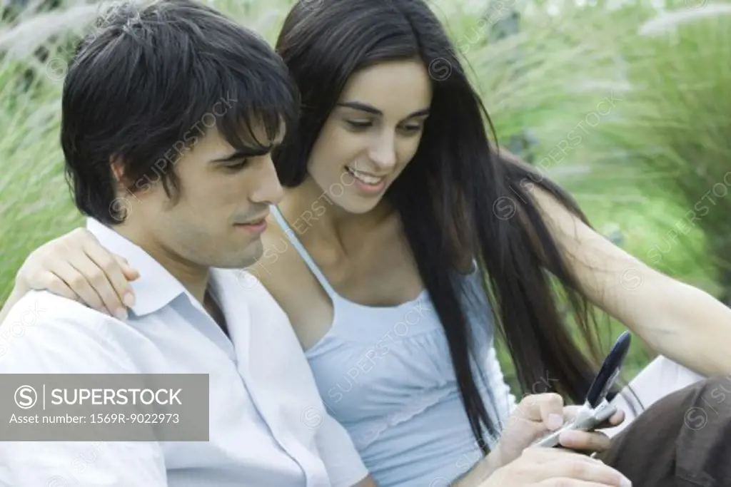 Young couple outdoors together, looking at cell phone
