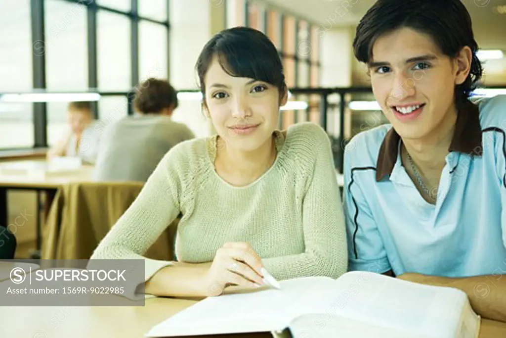 College students sitting at table in library, smiling at camera