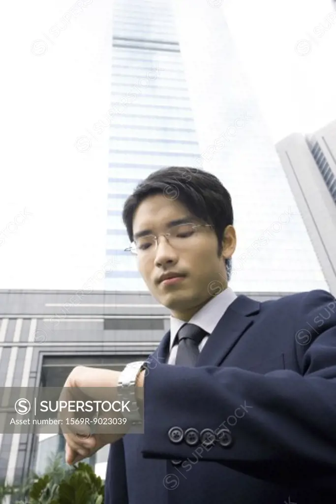 Businessman standing checking time on wristwatch, skyscraper in background