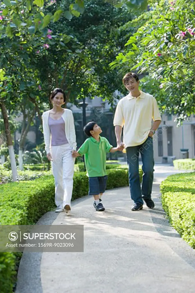 Boy walking hand in hand with parents, full length