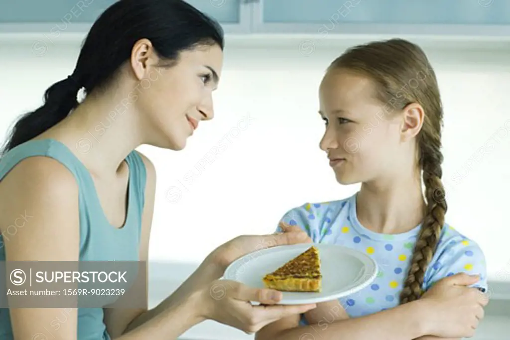 Girl crossing arms, looking at woman holding piece of quiche