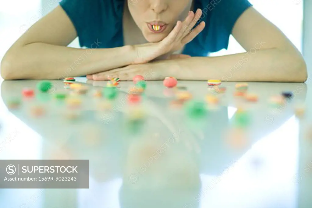 Table spread with candy, woman resting head on arms, holding piece of candy between teeth