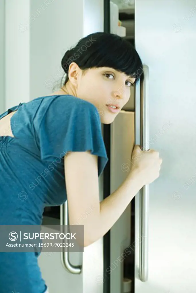 Woman bending over, opening refrigerator, looking over shoulder