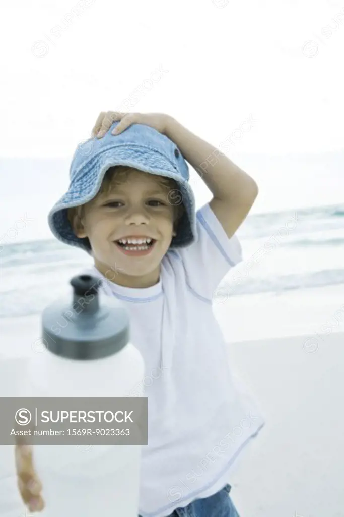 Boy holding up water bottle on beach