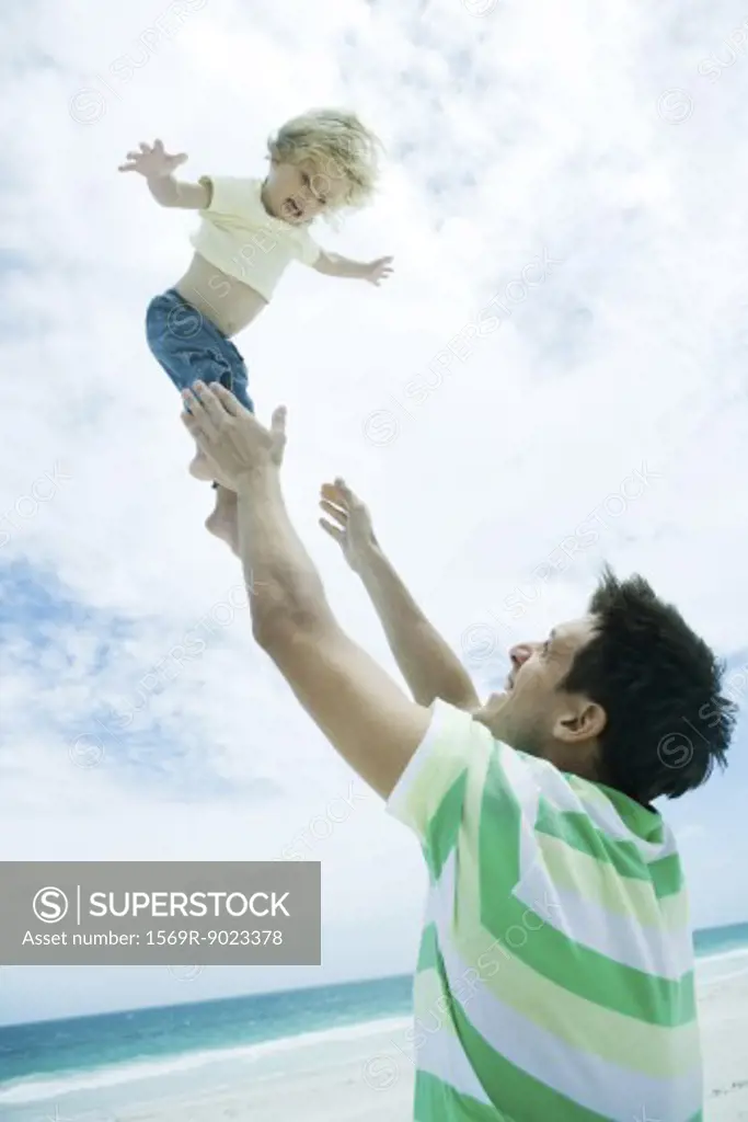Man throwing child into air on beach