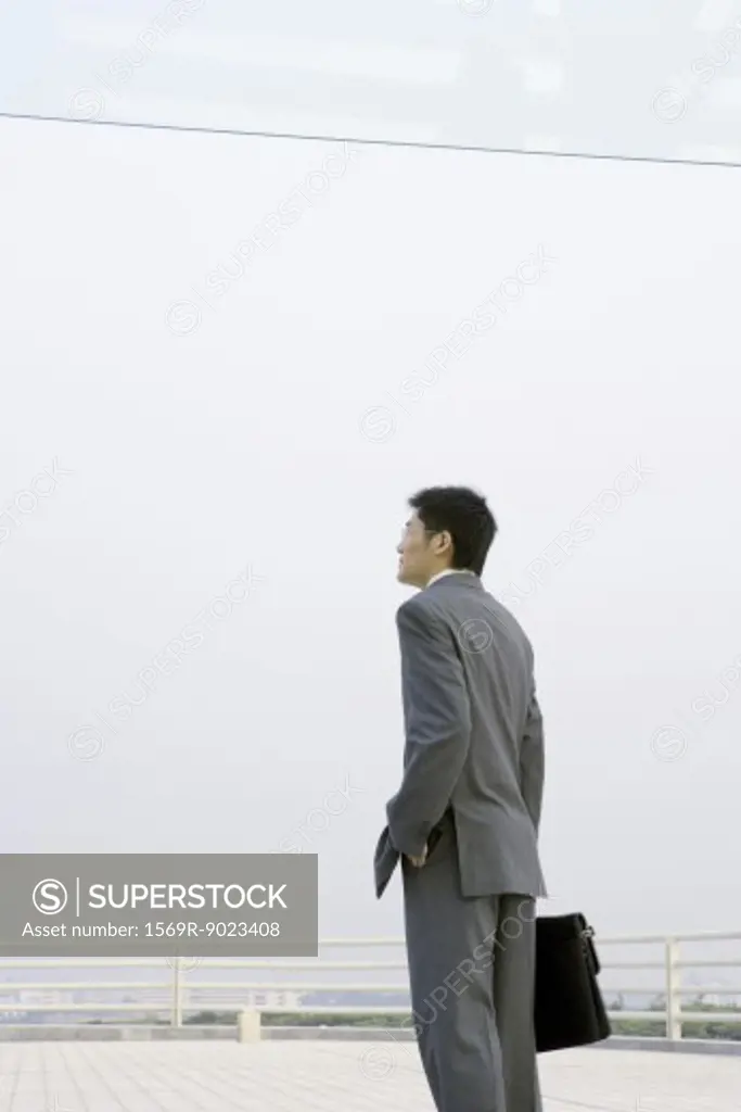 Businessman standing with briefcase, on office building terrace