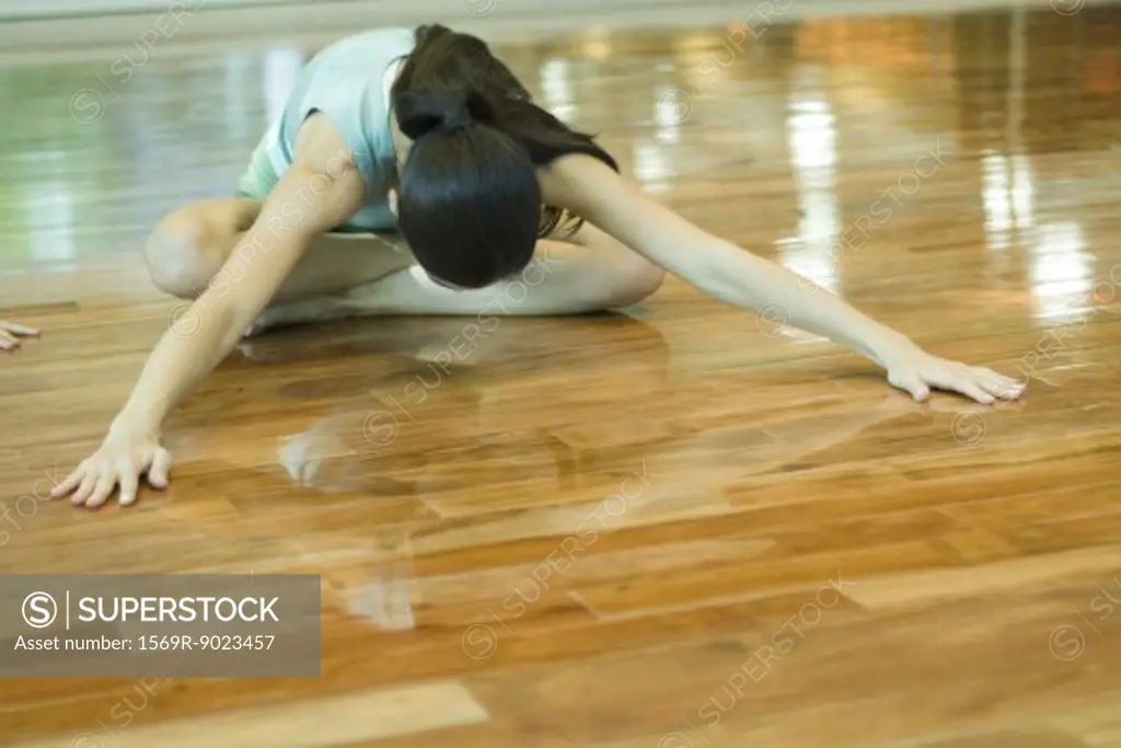 Young woman doing seating forward bend during exercise class