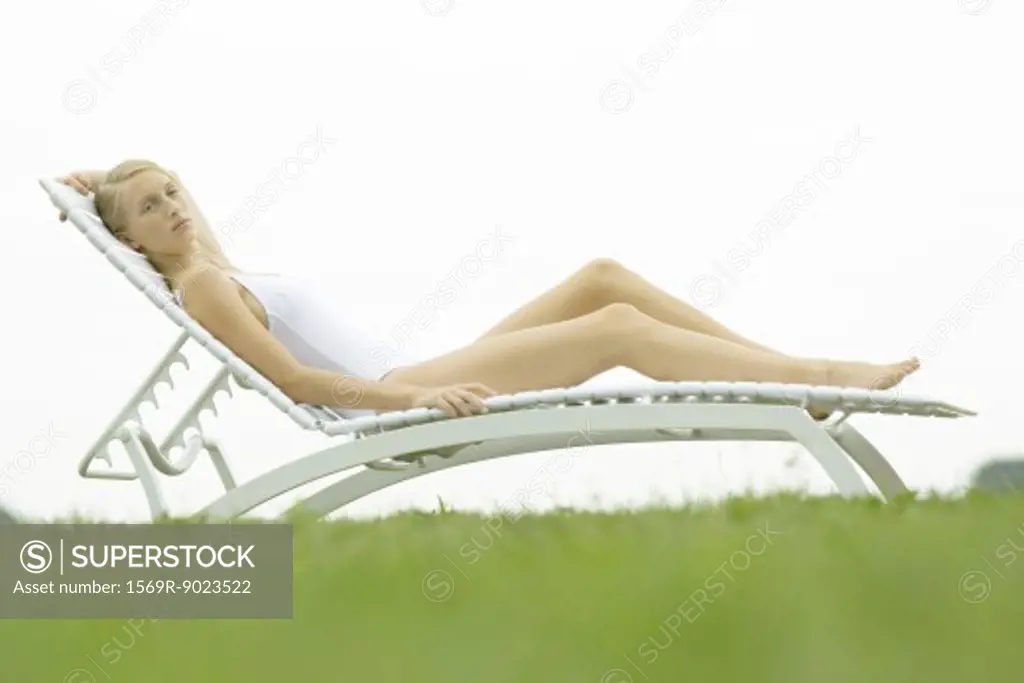 Teenage girl in swimsuit sitting on lounge chair