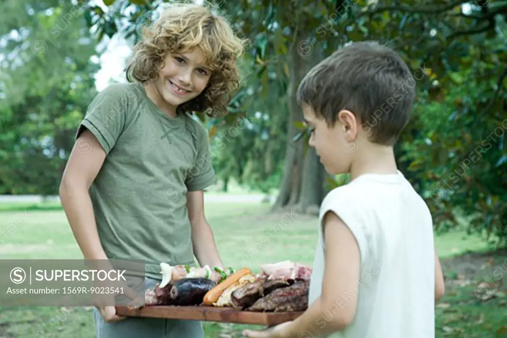 Two boys holding tray of grilled meats