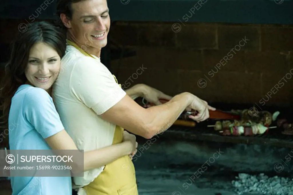 Couple having cookout, woman hugging man from behind