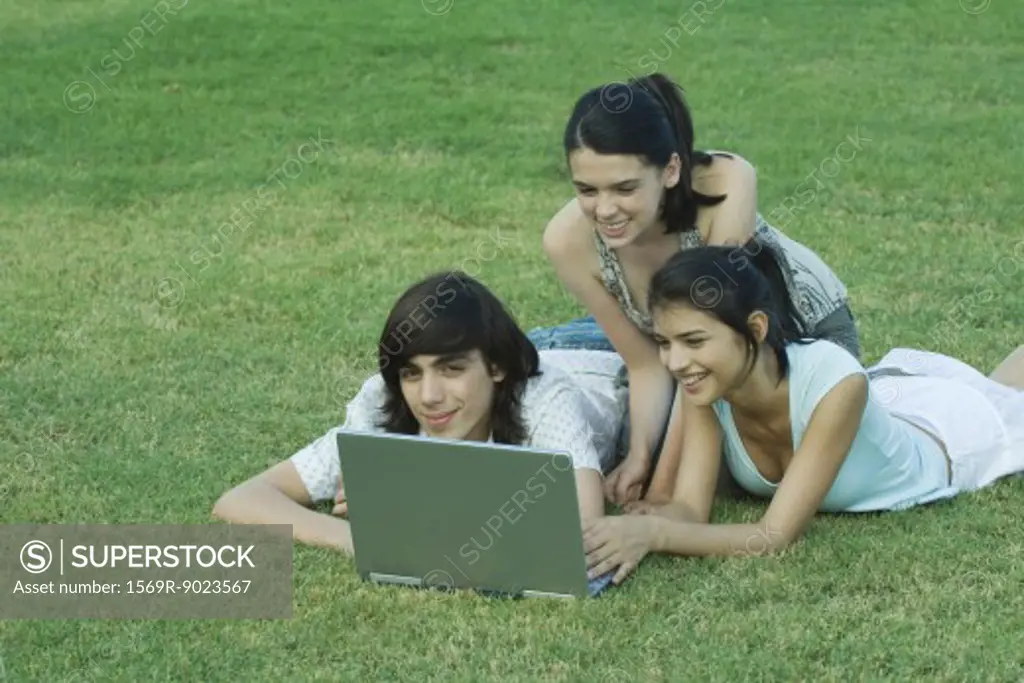 Group of young friends lying on grass together, using laptop